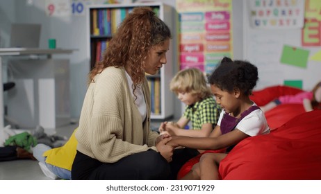 Young teacher cheering and calming upset African-American girl in kindergarten. Female teacher hug and comfort sad kid in nursery school - Powered by Shutterstock