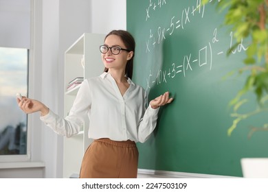 Young math’s teacher explaining mathematical equations near chalkboard in classroom