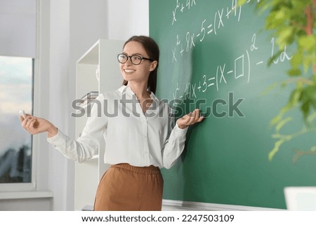 Young math’s teacher explaining mathematical equations near chalkboard in classroom