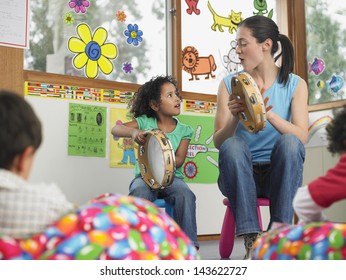 Young Teacher With Girl Playing Music In Classroom