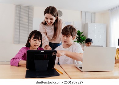 Young teacher guides diverse students with digital devices in modern classroom. Multiethnic elementary school setting - technology in education. - Powered by Shutterstock