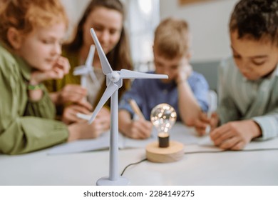 Young teacher with model of wind turbine learning pupils about wind energy. - Powered by Shutterstock