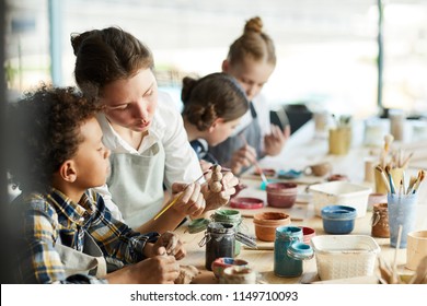 Young teacher showing one of pupils clay item and giving advice about painting it - Powered by Shutterstock