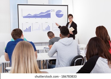 Young teacher teaching graphs drawn on whiteboard to college students in classroom - Powered by Shutterstock