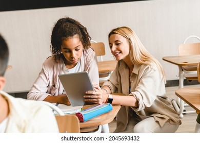 Young teacher tutor helping african-american girl students schoolchildren pupils with homework task math exam test at the school lesson class using digital tablet. - Shutterstock ID 2045693432