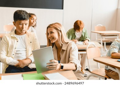 Young teacher tutor helping her students schoolchildren pupils with homework task math exam test at the school lesson class using digital tablet. - Powered by Shutterstock