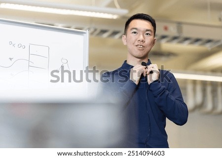 A young teaching instructor is adjusting his lavalier microphone in preparation for a online remote teaching session in front of the camera.