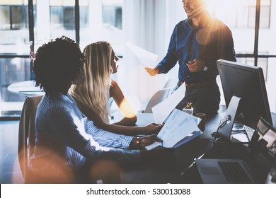 Young team of coworkers making great meeting discussion in modern coworking office.Hispanic businessman talking with two beautiful womans.Teamwork process.Horizontal,blurred background,sun effect