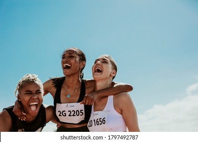 Young team of female athletes standing together and screaming in excitement. Diverse group of runners enjoying victory.