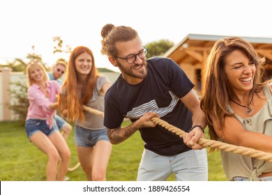 Young Team Having Fun Competing In Tug Of War Game While On Team Building Trip; Group Of Friends Having Fun While Participating In Rope Pulling Competition