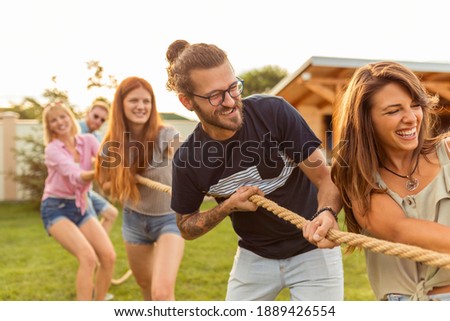 Young team having fun competing in tug of war game while on team building trip; group of friends having fun while participating in rope pulling competition