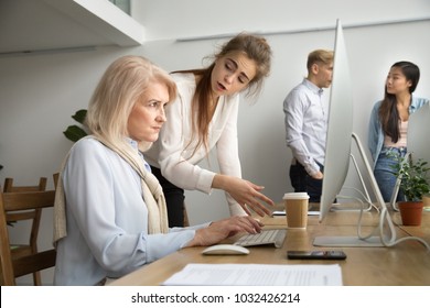 Young team leader correcting offended senior employee working on computer in office, female manager scolding aged old worker for mistake or incompetence, different generations and age discrimination