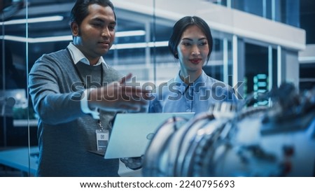Young Team of Multicultural Engineers Use Blueprints, Tablet and Laptop Computers, Analyze and Discuss How a Modern Electric Turbine Motor Works. High Tech Research Laboratory with Modern Equipment.