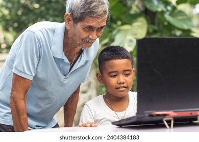 A young tech savvy Filipino boy teaches his grandfather how to use the laptop. Watching how to access the internet. Outdoor garden scene at home. - Powered by Shutterstock