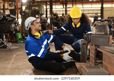 Young technician engineer or worker man in protective uniform had a leg accident lying on the floor in metal lathe factory. Safety colleague team helping him from accident. First aid training concept