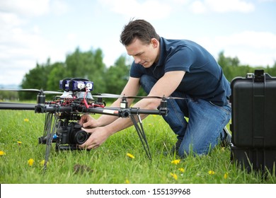 Young Technician Fixing Camera On UAV Helicopter In Park