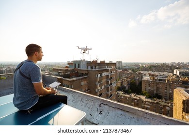 Young Technician Flying UAV Drone With Remote Control On Rooftop