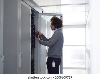 young IT technician using digital cable analyzer on server in large data center