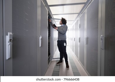 young IT technician using digital cable analyzer on server in large data center
