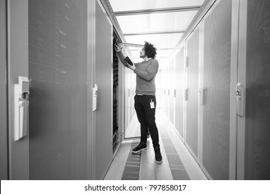 young IT technician using digital cable analyzer on server in large data center