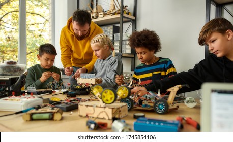 Young technicians building a robot, working with a wiring kit together with a male teacher at a stem robotics class. Inventions and creativity for kids. Selective focus. Web Banner - Shutterstock ID 1745854106