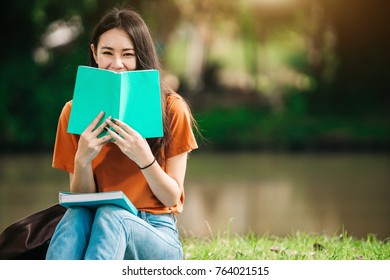 A Young Or Teen Asian Girl Student In University Smiling And Reading The Book And Look At The Tablet Or Labtop Computer In Summer Holiday.