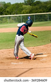 Young teen baseball batter in uniform swinging bat with referee in background.