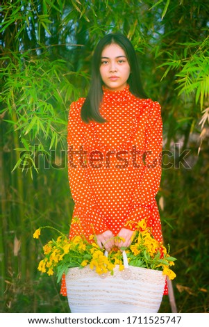 Young teen beautiful Asian lady wearing red vintage with hand carry bag of flowers on nature green tress background