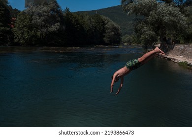 Young Teen Boy Jumping Flying And Diving In The River. Clear Blue Sky And Trees In Distance As A Natural Background.