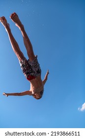 Young Teen Boy Jumping Flying And Diving In The River. Clear Blue Sky And Trees In Distance As A Natural Background.