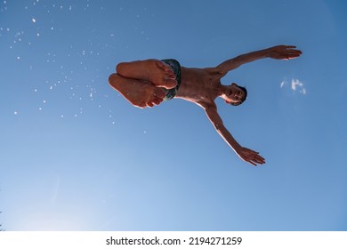 Young Teen Boy Jumping Flying And Diving In The River. Clear Blue Sky And Trees In Distance As A Natural Background.