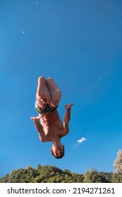 Young Teen Boy Jumping Flying And Diving In The River. Clear Blue Sky And Trees In Distance As A Natural Background.