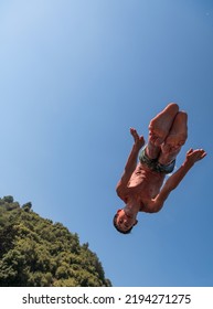 Young Teen Boy Jumping Flying And Diving In The River. Clear Blue Sky And Trees In Distance As A Natural Background.