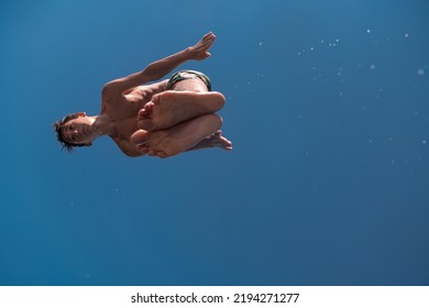 Young Teen Boy Jumping Flying And Diving In The River. Clear Blue Sky And Trees In Distance As A Natural Background.