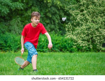 Young teen boy playing badminton in meadow with forest in background. Child with badminton rackets in hand. Kid have fun in summer park at day.