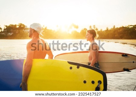 Young teen boy with a surfboard with his father go to the sea for surfing. They are smiling and enjoying a beautiful sunset light. Family active vacation concept.