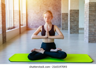 Young Teen Girl Practicing Yoga While Sitting In Lotus Pose On Mat In Studio. Padmasana Pose