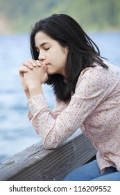 Young Teen Girl Sitting Quietly On Lake Pier, Praying