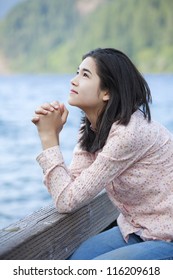 Young Teen Girl Sitting Quietly On Lake Pier, Praying