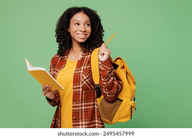 Young teen girl student wear brown yellow casual clothes backpack bag write down in exercise book notebook diary notes point finger aside isolated on plain green background High school college concept - Powered by Shutterstock