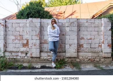 Young teen girl in white hoodie leaned on white brick wall and looking at the camera, outdoor photo