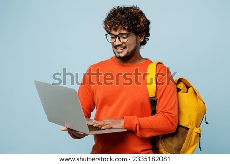 Young teen IT Indian boy student wear casual clothes backpack bag hold use work on laptop pc computer browsing internet isolated on plain pastel blue background. High school university college concept