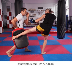 Young teen kickboxer training with his coach, hitting pads in the gym - Powered by Shutterstock