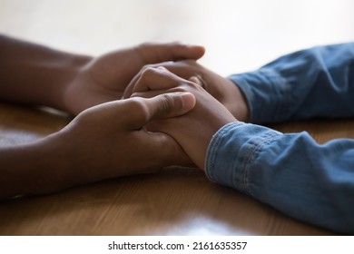 Young teen loving African couple holding arms on table surface. Guy touching hands of dark skinned Black girl, giving care, love, support, expressing tenderness, affection. Close up, cropped shot
