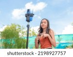 A young teen makes a video entry of the latest dance craze with her cellphone mounted on a tripod in their garden on a sunny afternoon.