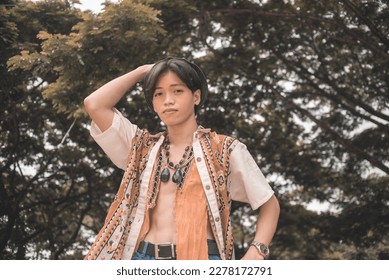 A young teenage asian hippie in an unbuttoned bohemian polo shirt posing outdoors. - Shutterstock ID 2278172791