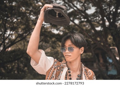 A young teenage asian hippie in an unbuttoned bohemian polo shirt and blue shades posing outdoors. - Shutterstock ID 2278172793