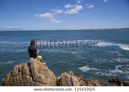 young teenage boy fishing by the sea on some rocks