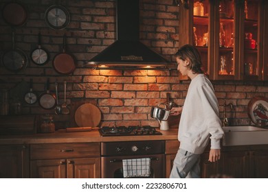 Young teenage boy with long hair in morning routine and preparing on kitchen at home. Stylish zoomer gen Z in casual clothing celebrates new year lights holidays garlands eve xmas enjoying cooking - Shutterstock ID 2232806701