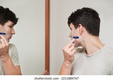 A Young Teenage Boy Shaves For The First Time, Looks Carefully In The Mirror And Shaves Off A Small Beard. A Teenager Shaves